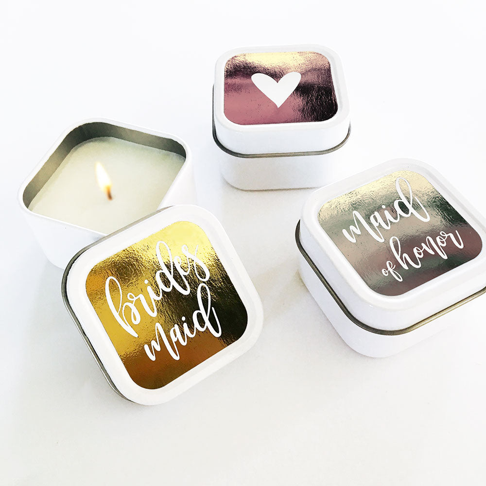 Small square tins with candles inside. The lid has three different colored stickers with the words: bridesmaid, maid of honor, and a heart.